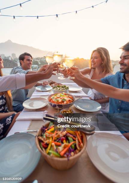 groep vrienden die een maaltijd in openlucht hebben. ze vieren het met een toast met witte wijn. - restaurant patio stockfoto's en -beelden