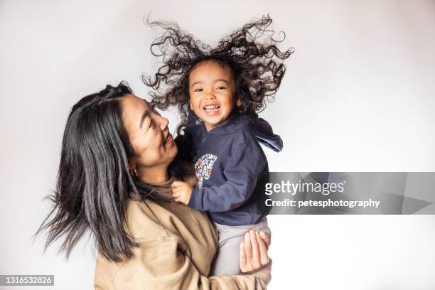 een jong meisje met een grote glimlach en kroeshaar in de lucht die door haar moeder wordt gedragen - big hair stockfoto's en -beelden