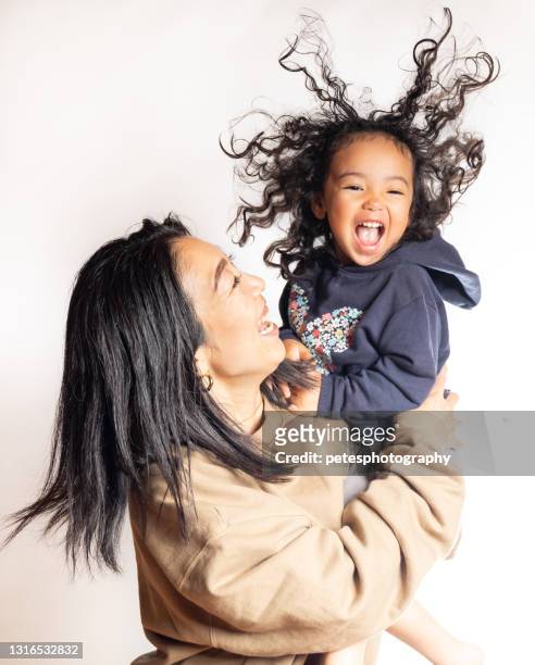 een jong meisje met een grote glimlach en kroeshaar in de lucht die door haar moeder wordt gedragen - big hair stockfoto's en -beelden