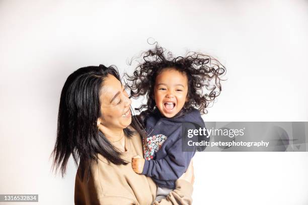 een jong meisje met een grote glimlach en kroeshaar in de lucht die door haar moeder wordt gedragen - big hair stockfoto's en -beelden