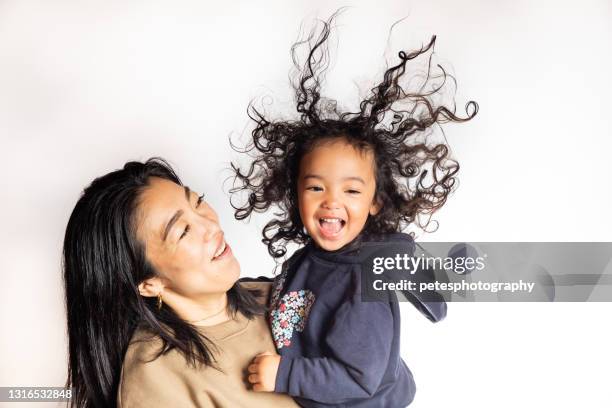 een jong meisje met een grote glimlach en kroeshaar in de lucht die door haar moeder wordt gedragen - big hair stockfoto's en -beelden