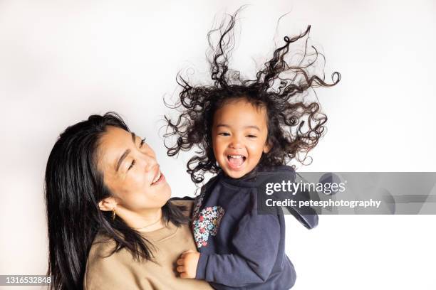 a young girl with a big smile and frizzy hair in the air being carried by her mother - static electricity stock pictures, royalty-free photos & images