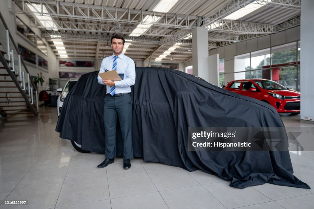 Vendedor de pie junto a un coche cubierto en el concesionario