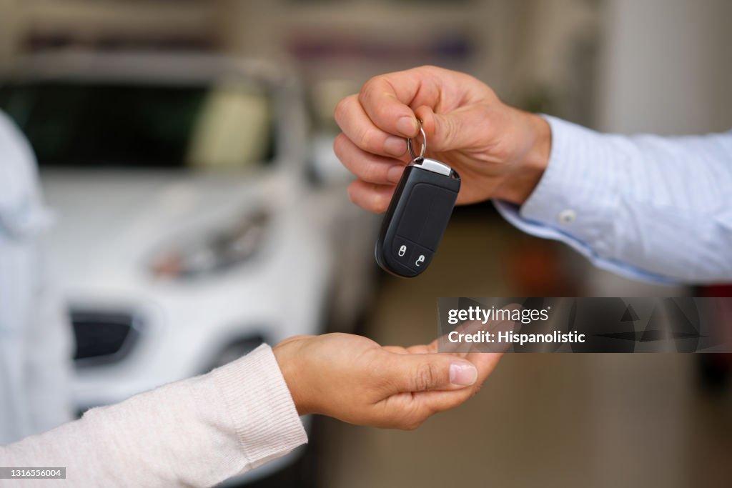 Close-up on a salesman giving the keys to their new car to a couple at the dealership
