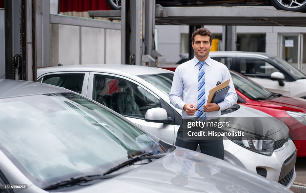 Retrato de um vendedor trabalhando na concessionária mostrando carros ao ar livre