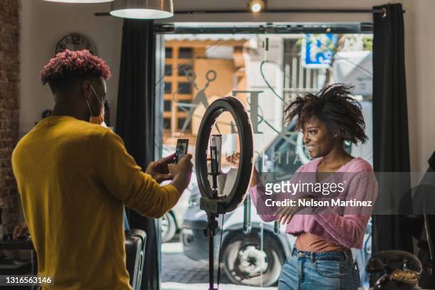 brazilian black hairstylist taking a photo to a black woman blogger. social media influencer concept - content stock-fotos und bilder