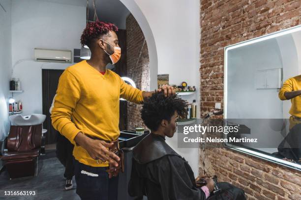 black brazilian hairstylist cutting the hair of a black woman. he is wearing a mask as protection from covid19 - hairdressers black woman stockfoto's en -beelden