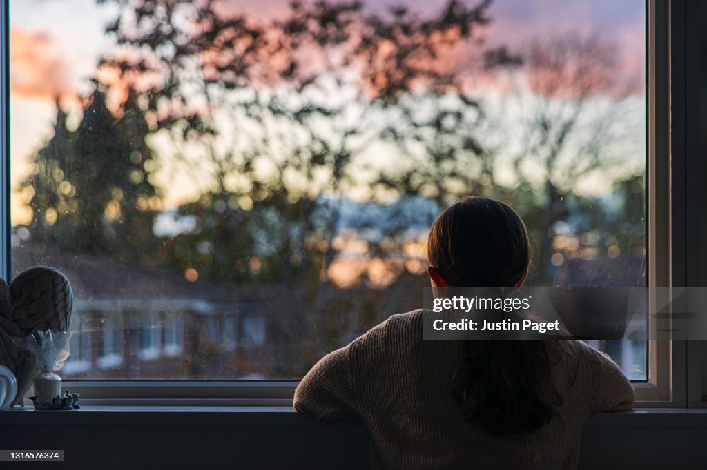 Rear view shot of a young girl looking out of her window at sunset