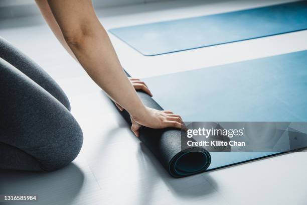 asian woman rolling up yoga mat in a yoga studio - pilates stockfoto's en -beelden