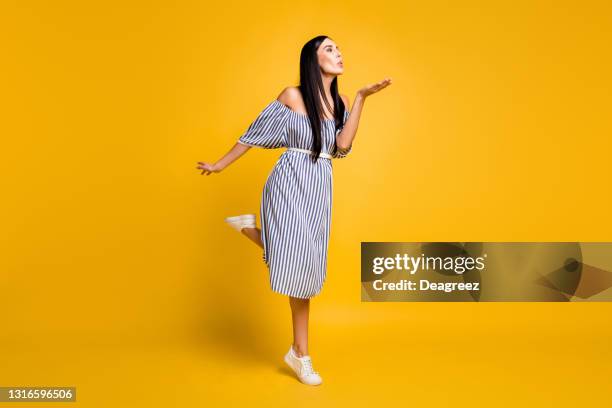 Full length photo of charming sweet young lady wear striped dress sending kiss arm empty space isolated yellow color background