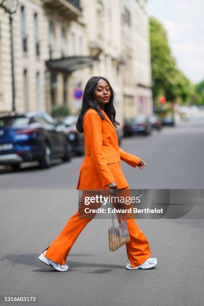 Carrole Sagba @linaose wears gold earrings, an orange belted Blazer jacket and matching suit flared Warehouse pants, white New balance sneakers, a...