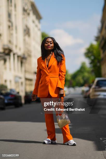 Carrole Sagba @linaose wears gold earrings, an orange belted Blazer jacket and matching suit flared Warehouse pants, white New balance sneakers, a...