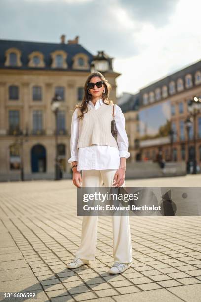 Amanda Derhy @amanda_jashley wears black sunglasses, pearls earrings, an oversized shirt, large flared pants, a beige sleeveless ribs wool pullover,...