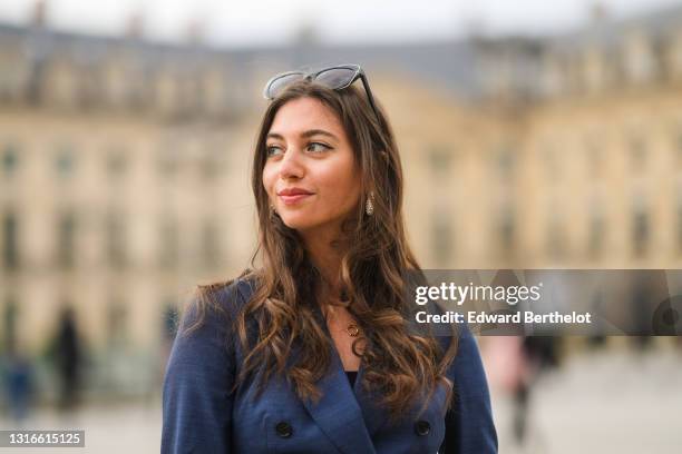 Amanda Derhy @amanda_jashley wears black sunglasses, pearls earrings, a gold pendant necklace, a black t-shirt, a navy blue long blazer jacket, on...