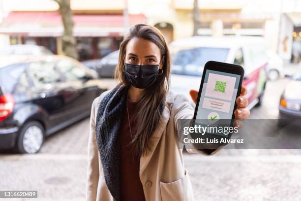 woman with mask showing digital vaccine certificate on phone - system demonstration stock pictures, royalty-free photos & images