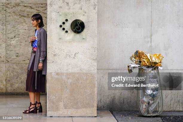 Model wears a pin, earrings, rings, bracelets, a colorful top, a brown belt, a grey jacket with lace inserts, a deep purple and grey skirt with lace...