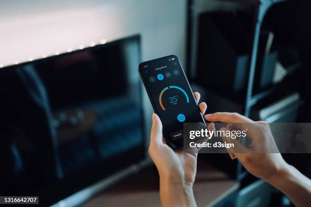 close up of woman's hand setting up the intelligent home system with smartphone, remote-controlling the thermostat of smart air-conditioner in the living room of her smart home. smart living. lifestyle and technology - control room monitors stockfoto's en -beelden