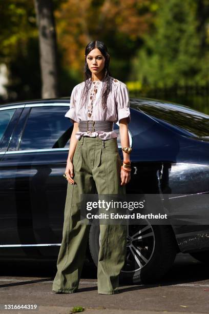 Model wears rings, bracelets, a gathered pinstriped top, a large black belt, khaki wide legs and full length pants, black sandals, outside Chloe,...