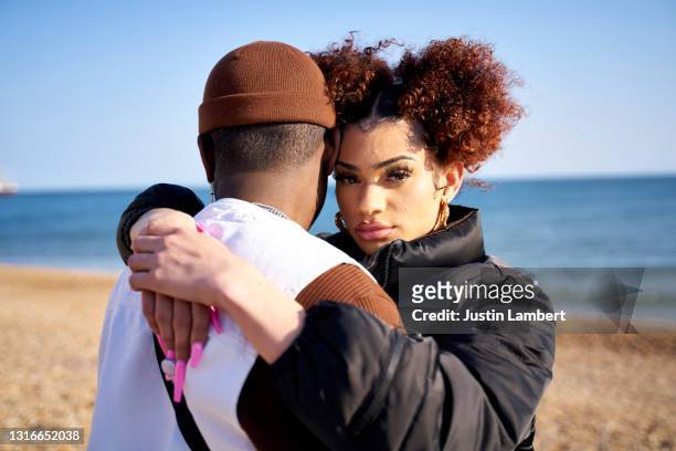 couple embracing at the beach looking to camera - bonding stock pictures, royalty-free photos & images