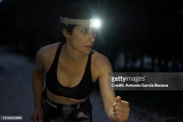 woman in sportswear trains to run alone at night with lamp on her head - head torch stock-fotos und bilder