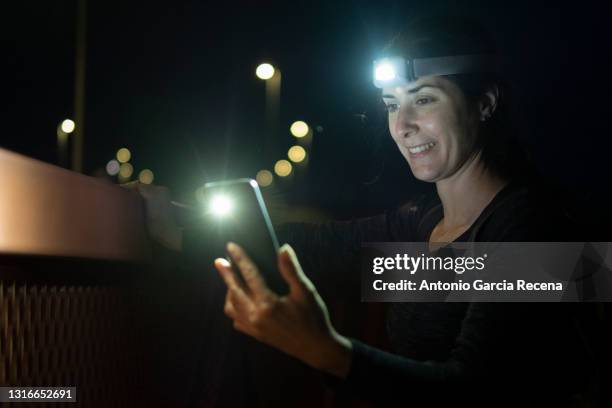 attractive woman starts a night excursion with her backpack and headlamp, road lights in the background. note: taken in ambient light, this image contains noise. - flashlight stock-fotos und bilder