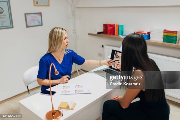de deskundigheidsde vrouwelijke dermatoloog die de verwijzingsfoto gebruikt om aan haar jonge vrouwelijke patiënt uit te leggen hij behandelingsprocedure van mesotherapie - plastische chirurgie stockfoto's en -beelden