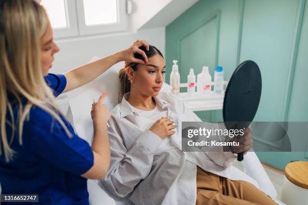 junge frau beobachtet sich im spiegel, nachdem die kosmetikerin beendet verfahren der stirnheben mit einem botox - plastische chirurgie stock-fotos und bilder