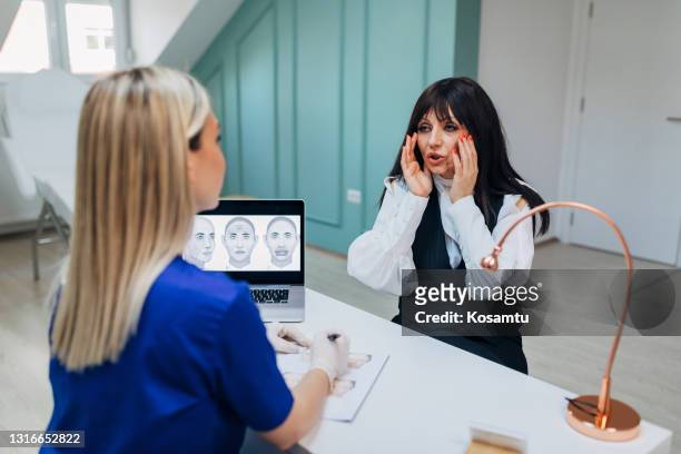 mature female client visiting the clinic, to reduce her eyes wrinkles with a botox treatment - dermatologists talking to each other patient stock pictures, royalty-free photos & images