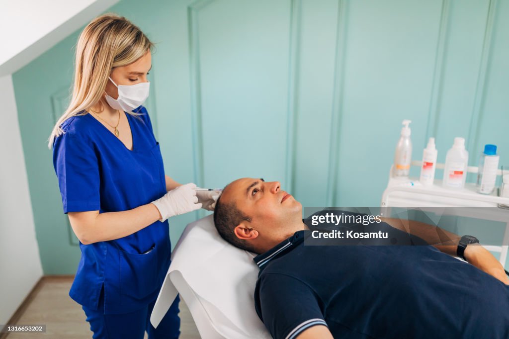 Beautician using on her mid adult male patient the new way for a hair growth while injecting the collagen and vitamins with syringe
