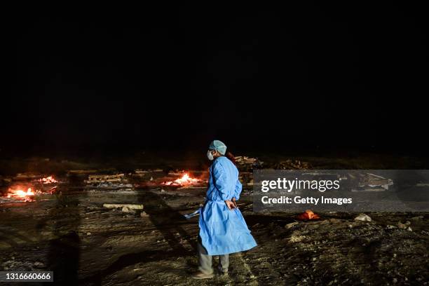 Medical worker watches cremations of the bodies of Covid-19 victims on the banks of the Ganges river May 06, 2021 in Allahabad, Uttar Pradesh, India....