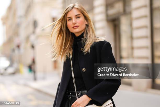 Xenia Adonts wears a black wool turtleneck ribs open neck pullover, a long black Gucci coat, black shiny leather pants, on April 30, 2021 in Paris,...