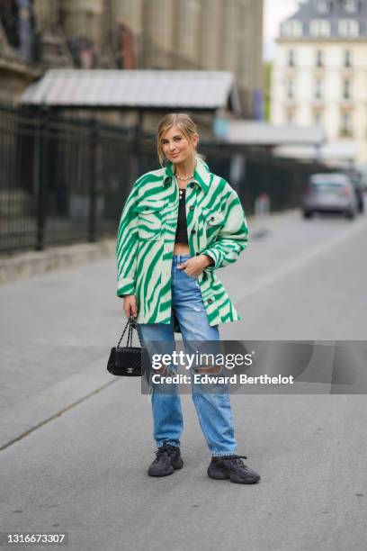 Xenia Adonts wears red and gold earrings, a multicolors pearls necklace, silver and gold chain pendant necklaces, a black crop top, a green and pale...