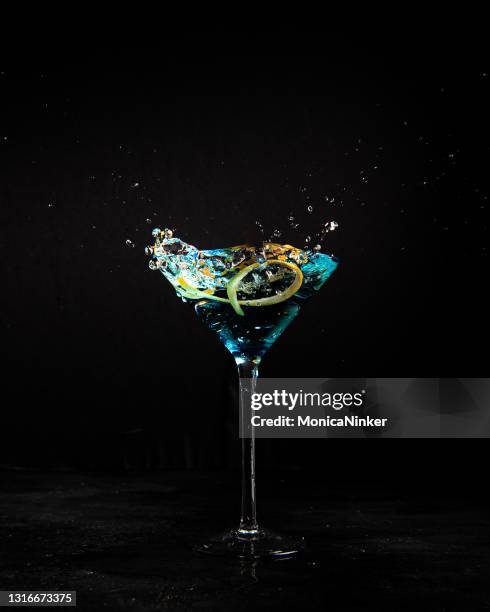 blauer martini mit orangen scheibe spritzen auf der oberseite - blue martini glasses stock-fotos und bilder