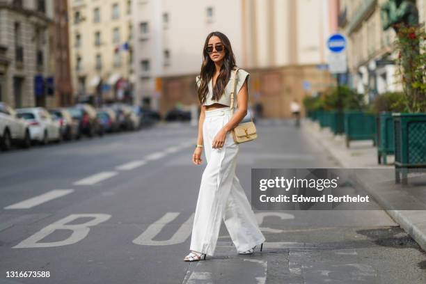 Tamara Kalinic wears gold Bottega Veneta sunglasses, a gold chain pendant necklace, a pale gray Jacquemus V-neck collar crop top with epaulets, white...