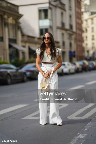 Tamara Kalinic wears gold Bottega Veneta sunglasses, a gold chain pendant necklace, a pale gray Jacquemus V-neck collar crop top with epaulets, white...