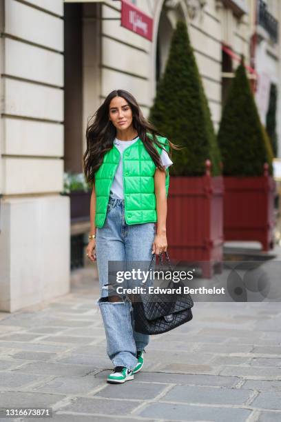 Tamara Kalinic wears gold earrings, a gold chain pendant necklace, a black t-shirt, a white t-shirt with a slogan 'with me', a green shiny leather...