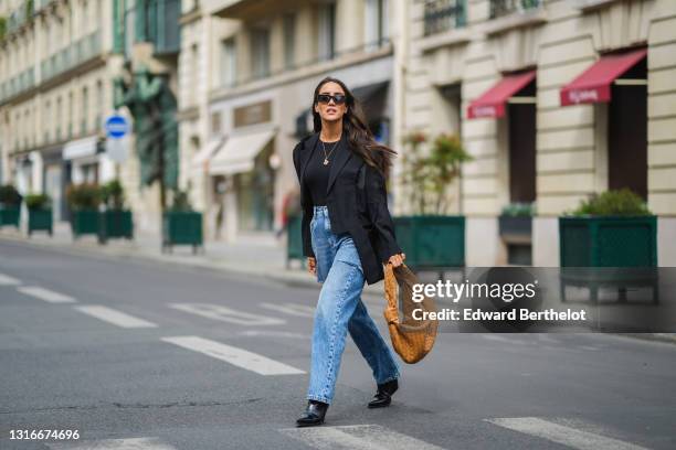 Tamara Kalinic wears black Sestini sunglasses, gold earrings, a black t-shirt, a black oversized ripped Margiela blazer jacket, a gold ring, blue...