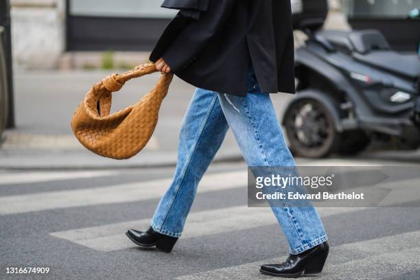 Tamara Kalinic wears a black oversized ripped Margiela blazer jacket, blue faded denim oversized Margiela jeans pants, a brown shiny leather braided...
