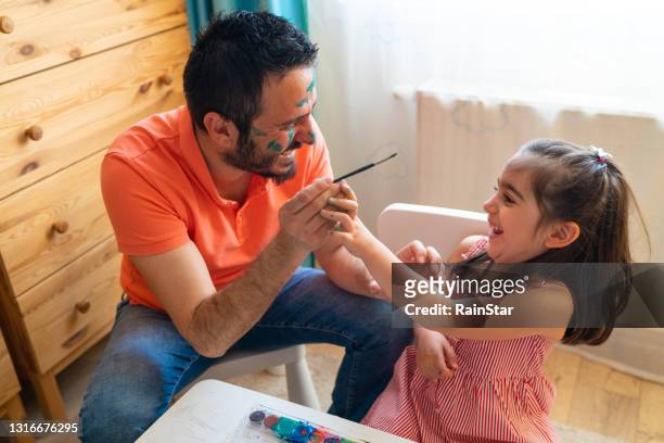 le père, dont le visage est peint par sa petite fille, tente de peindre le visage de sa petite fille - makeup in rain photos et images de collection