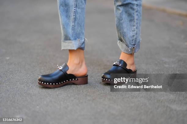 Xenia Adonts wears blue faded denim ripped rolled-up boyfriend jeans Ksubi pants, black shiny leather nailed Hermes mules block heels shoes, on April...