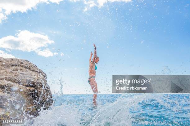 sea spray and water droplets from kids jumping into the sea during summer vacation. young teenage girl diving from rocks into the sea - cliff dive stock pictures, royalty-free photos & images