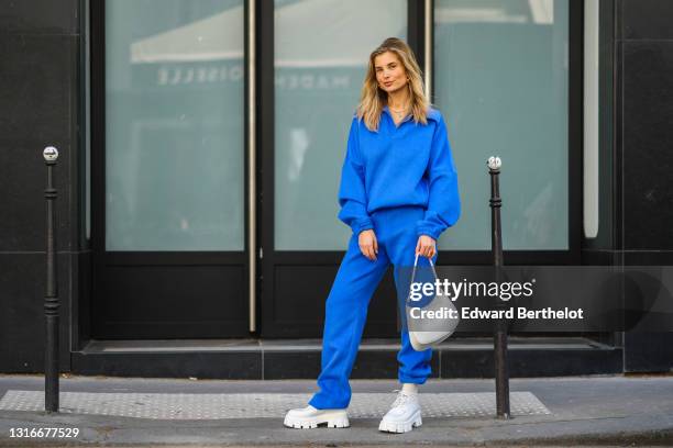 Xenia Adonts wears a pearls necklace, a royal blue V-neck sweater with matching large Shabderb jogger sport pants, a gold watch, a gold ring, a white...