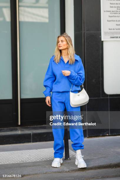 Xenia Adonts wears a pearls necklace, a royal blue V-neck sweater with matching large Shabderb jogger sport pants, a gold watch, a gold ring, a white...
