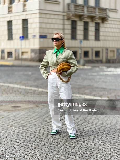 Justyna Czerniak wears black sunglasses from Loewe, gold earrings, a green crop-top shirt from One-Shirt, a beige striped short blazer jacket from...