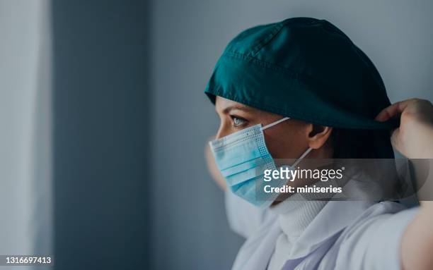female surgeon putting on surgical cap in operating room - protective face mask side stock pictures, royalty-free photos & images