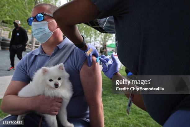 Man holds his emotional support dog, named 'Rhea,' as he receives a dose of the Johnson & Johnson coronavirus vaccine during a walk-up clinic at the...