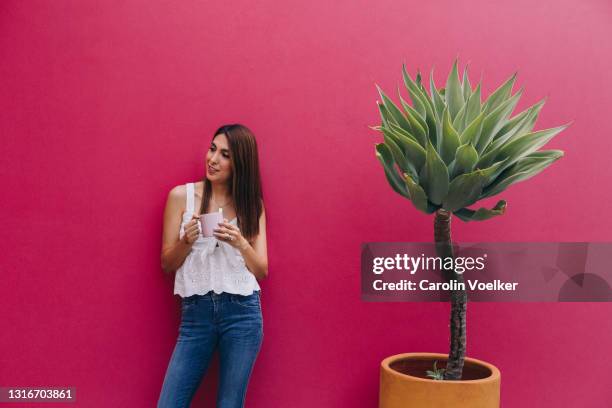 three quarter length portrait of woman in jeans holding a coffee cup in front of a pink background - three quarter front view stockfoto's en -beelden