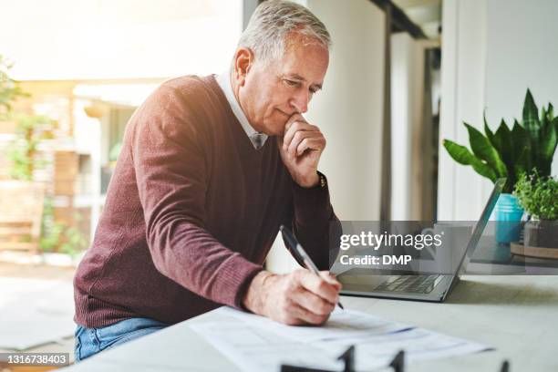 ontsproten van een hogere mensenzitting alleen en gebruikend zijn laptop om zijn financiën thuis te berekenen - erfenis stockfoto's en -beelden