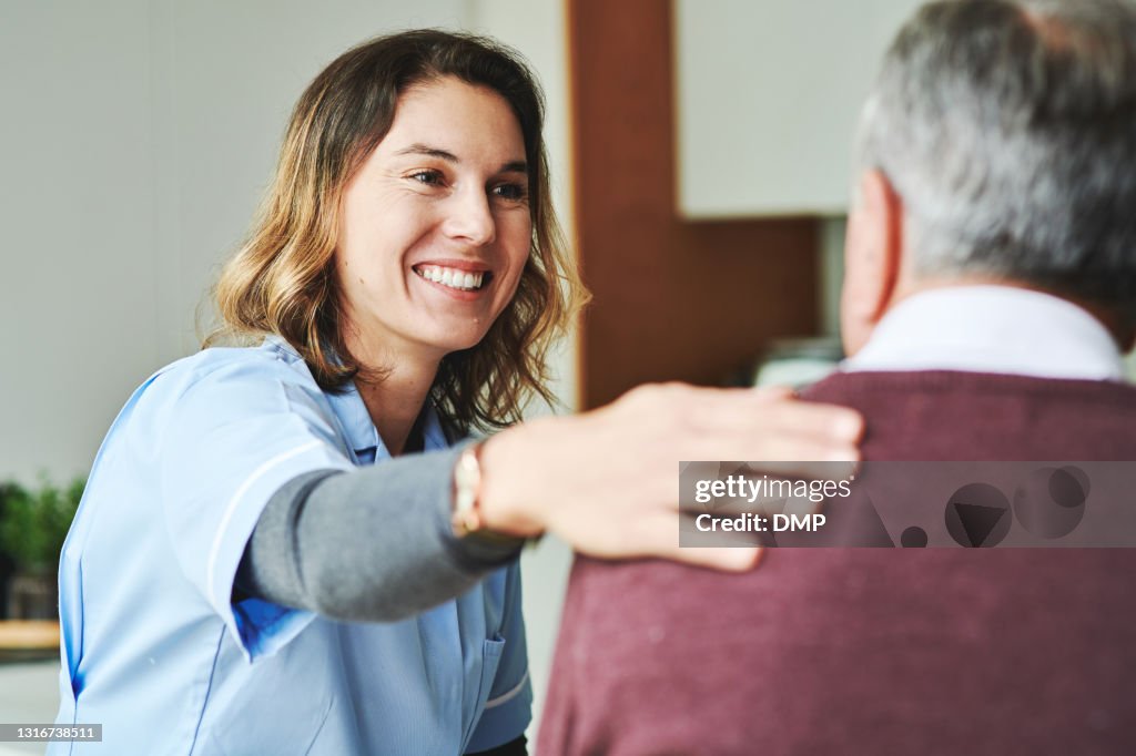 Shot of an attractive young nurse sitting and bonding with her senior patient in his kitchen at home