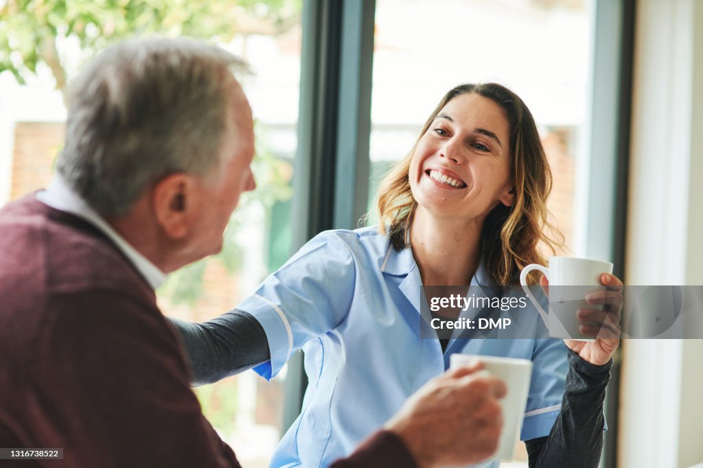 Shot of an attractive young nurse sitting and bonding with her senior patient in his kitchen at home